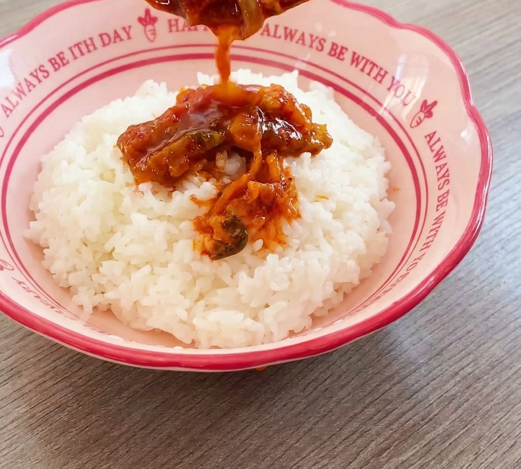 분홍색 그릇에 담긴 밥 위로 볶은 김치 소고기를 얹는 모습.