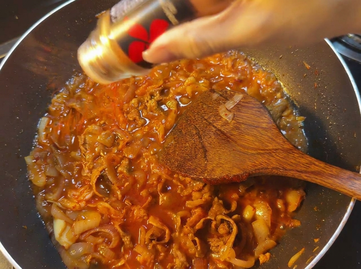 보글보글 끓는 소스 위로 고춧가루를 솔솔 뿌려 색감과 매운맛을 더하는 모습.