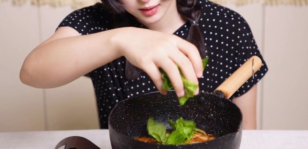 끓는 팬 위에 신선한 초록 채소를 뿌리는 모습.