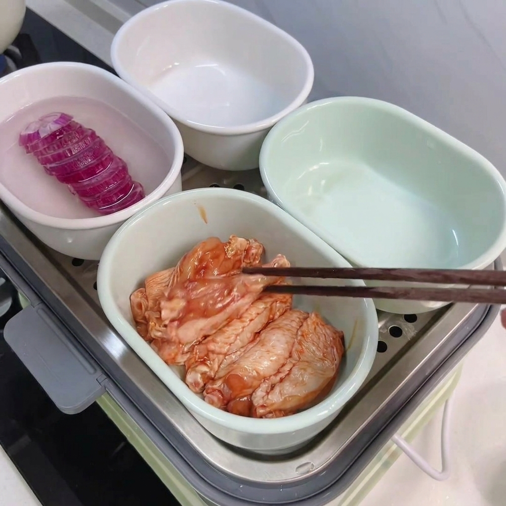 젓가락을 이용해 양념된 닭날개를 접시에 옮겨 담는 모습.
