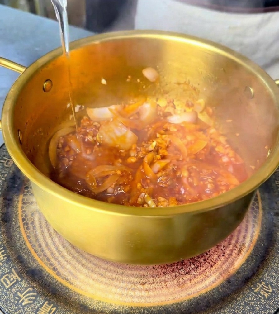 매콤한 양념 재료가 담긴 냄비에 깨끗한 물을 붓는 모습.