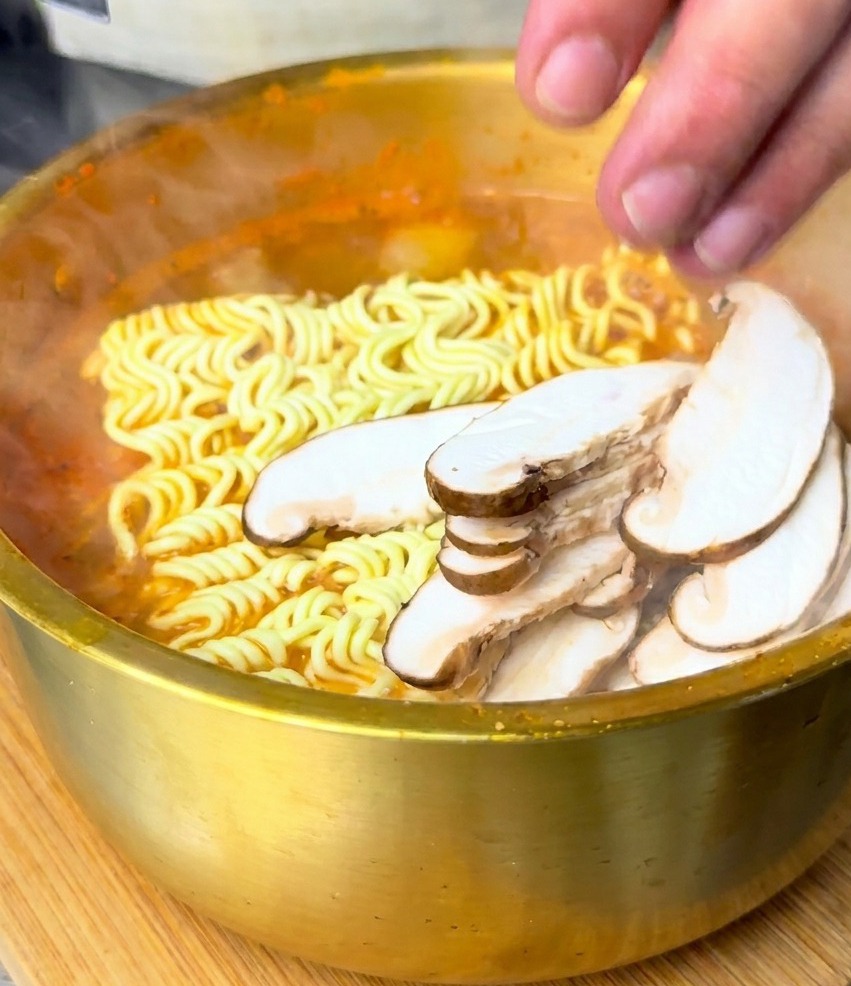 끓는 라면 위에 손질한 표고버섯과 팽이버섯을 올리는 모습.