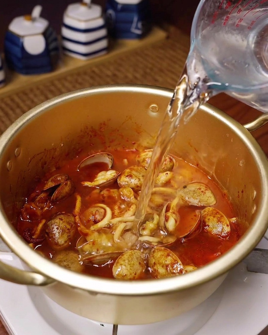 양념된 해산물이 담긴 냄비에 유리 계량컵으로 물을 붓는 모습