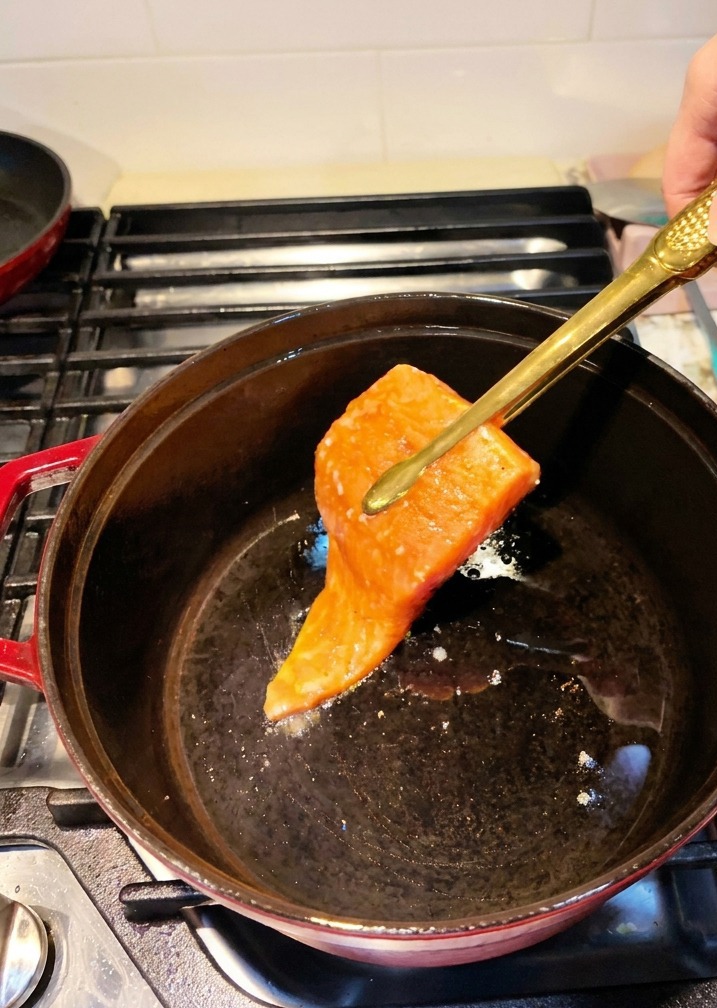예열된 무쇠 솥에 집게로 연어 필렛을 올리는 모습.