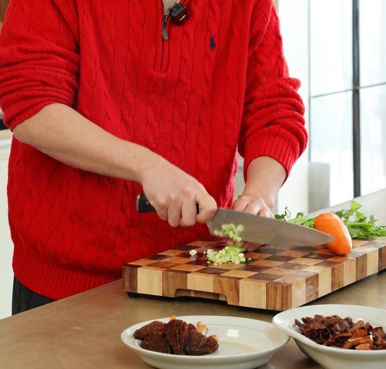나무 도마 위에서 셀러리와 당근을 일정한 크기로 다지고 있는 모습.