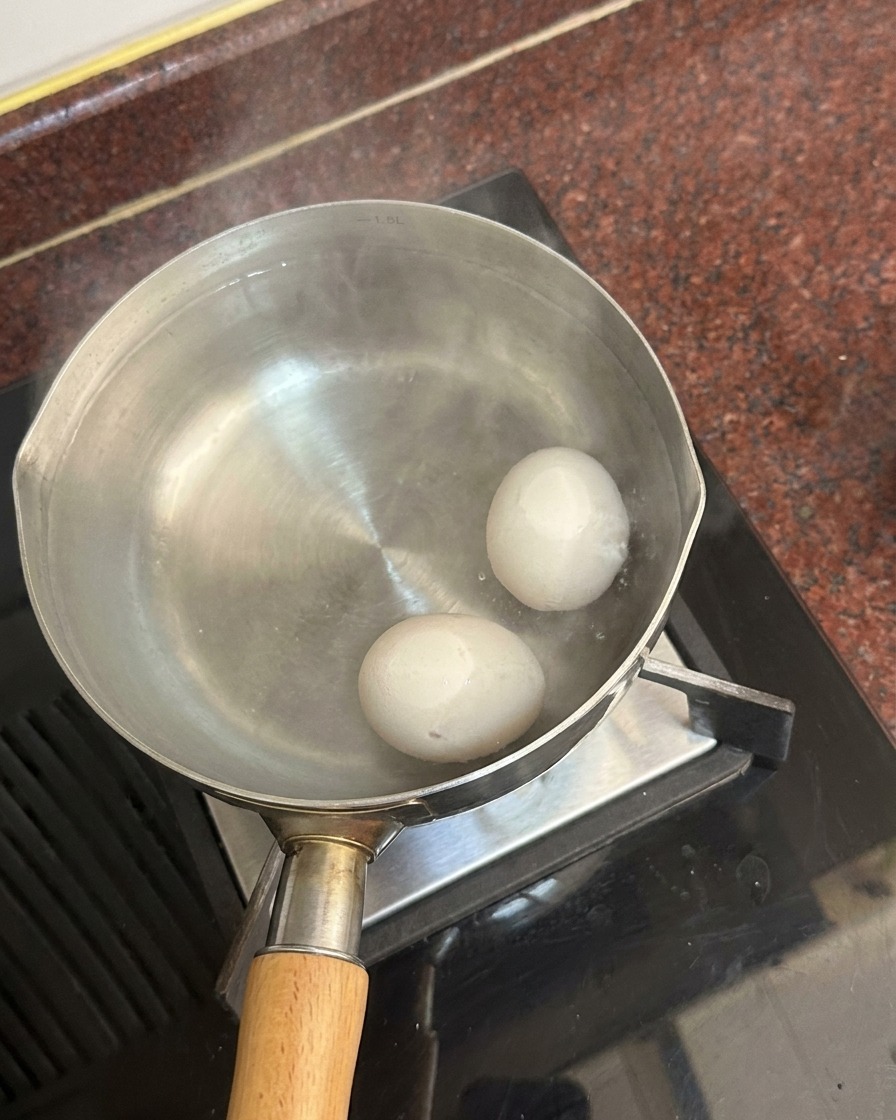 김이 모락모락 나는 뜨거운 물이 담긴 냄비 바닥에 놓인 두 알의 흰 달걀.