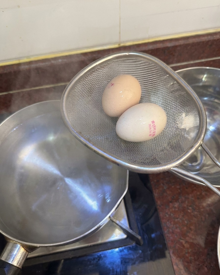 체에 받쳐진 달걀을 뜨거운 물에서 건져내어 얼음물 볼로 옮기려는 모습.