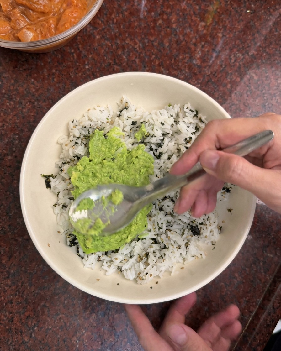 흰 그릇에 담긴 밥과 김가루 위에 초록색 아보카도 페이스트를 숟가락으로 펴 바르는 모습.