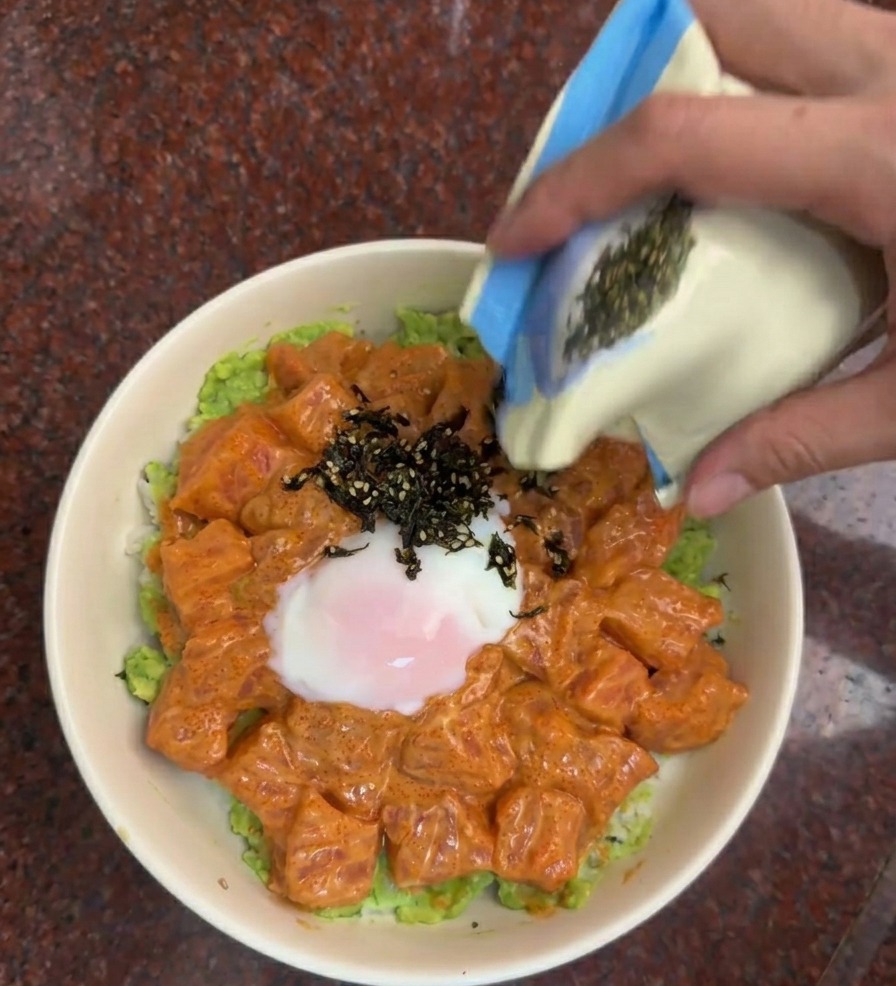 완성된 덮밥 위에 김가루와 검은깨를 뿌려 마무리하는 손.