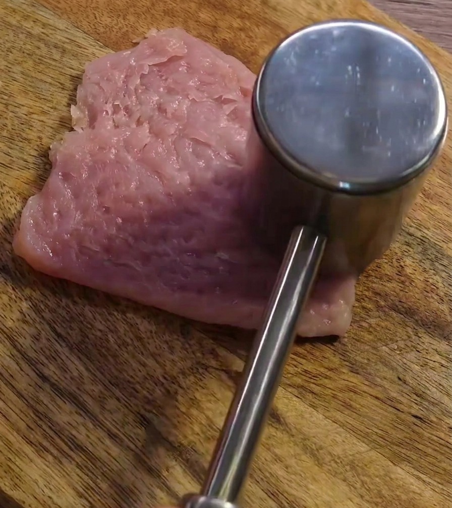 도마 위의 돼지고기를 고기 망치로 두드려 펴는 모습