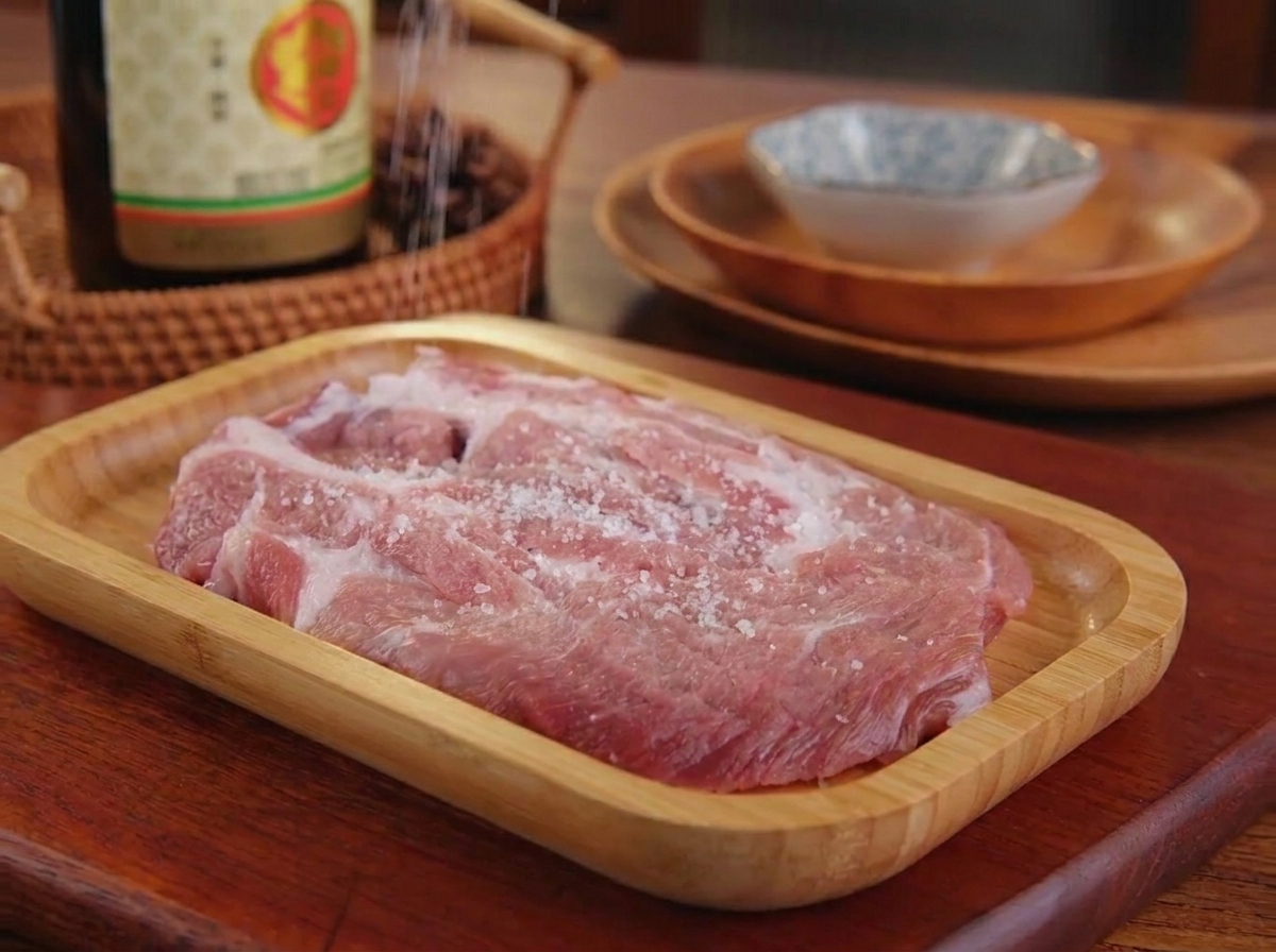 목재 쟁반 위에 놓인 생돼지고기에 소금과 후추를 골고루 뿌리는 모습