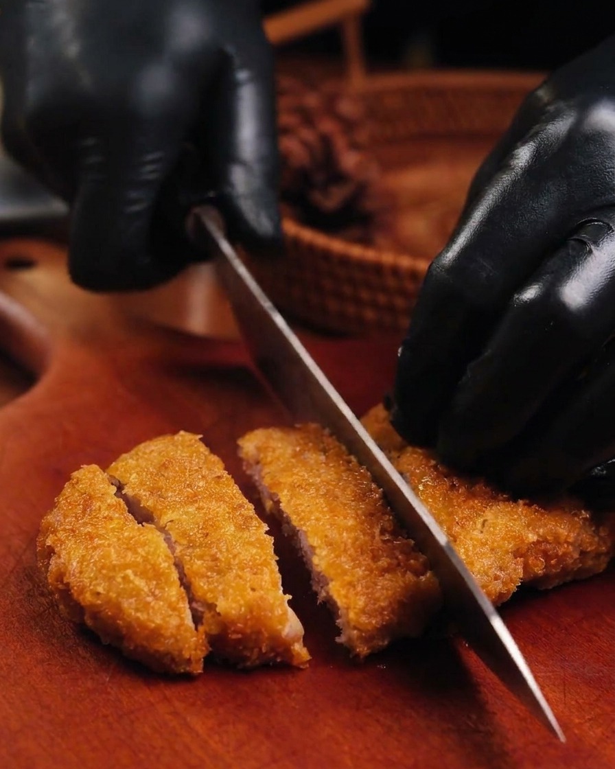도마 위 황금빛 돈가스를 잘 드는 칼로 썰고 있는 모습.
