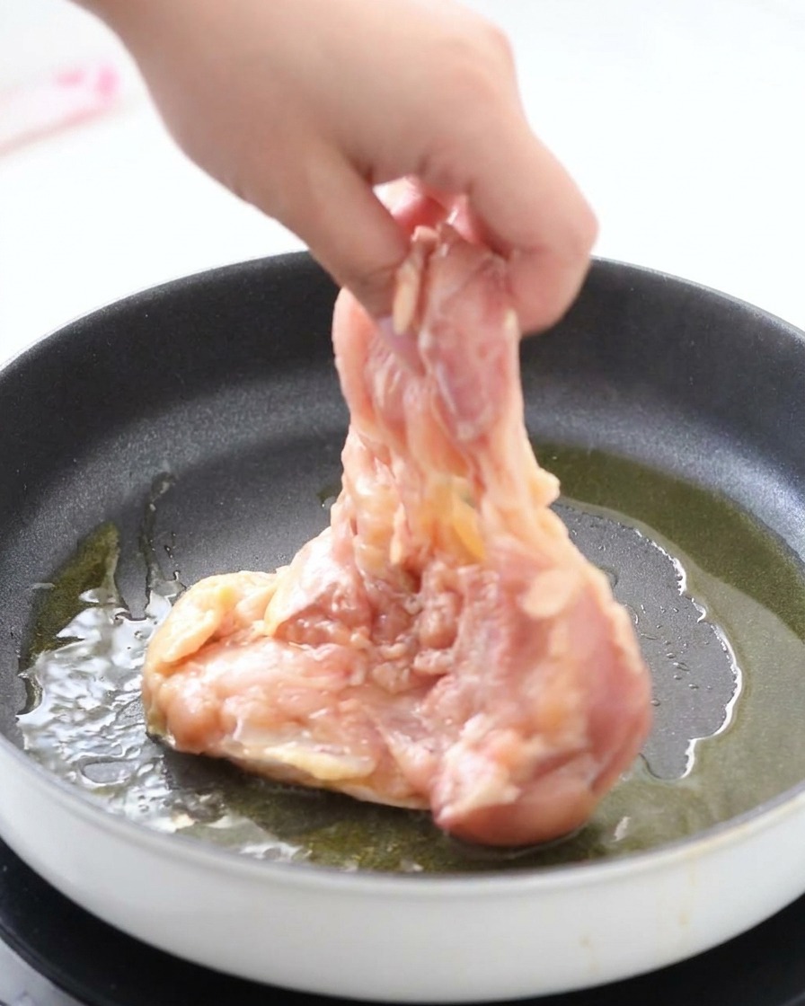 기름을 두른 뜨거운 팬에 마리네이드된 닭다리살을 껍질이 아래로 가도록 조심스럽게 올리는 모습.