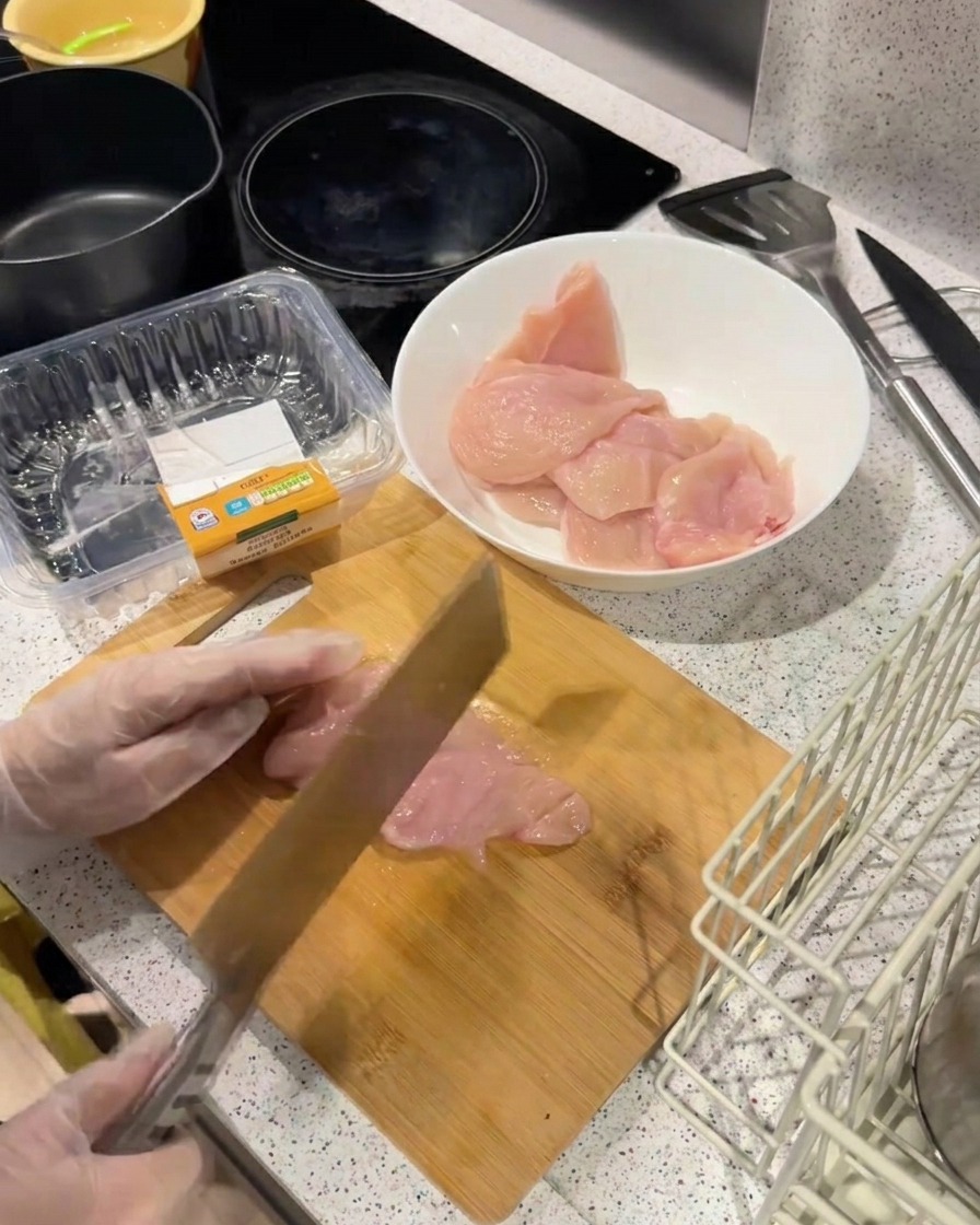 무거운 칼등으로 도마 위의 닭가슴살을 두드려 얇고 평평하게 펴는 모습