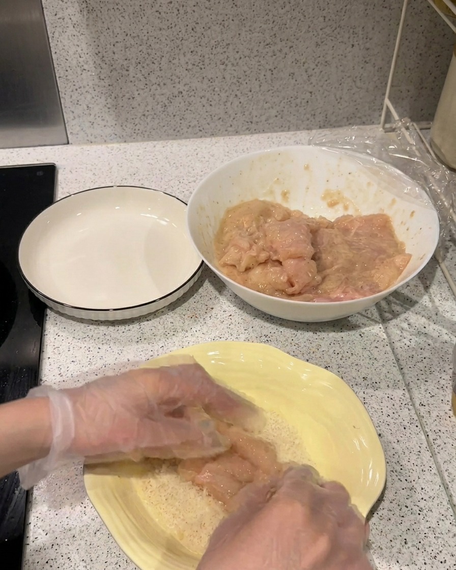 밑간한 고기를 노란 접시에 담긴 바삭한 빵가루 위에 올리고 누르는 모습