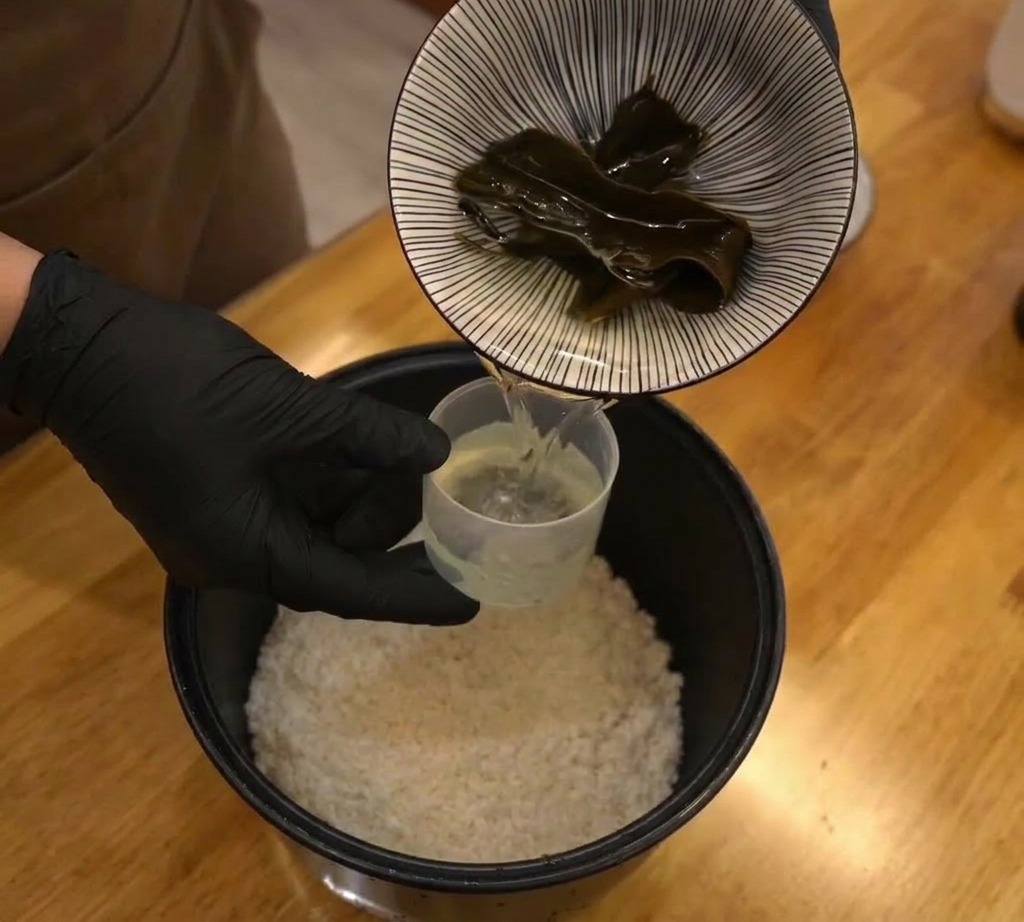 생쌀과 물이 담긴 밥솥 솥 안에 건다시마 한 조각을 넣는 모습.