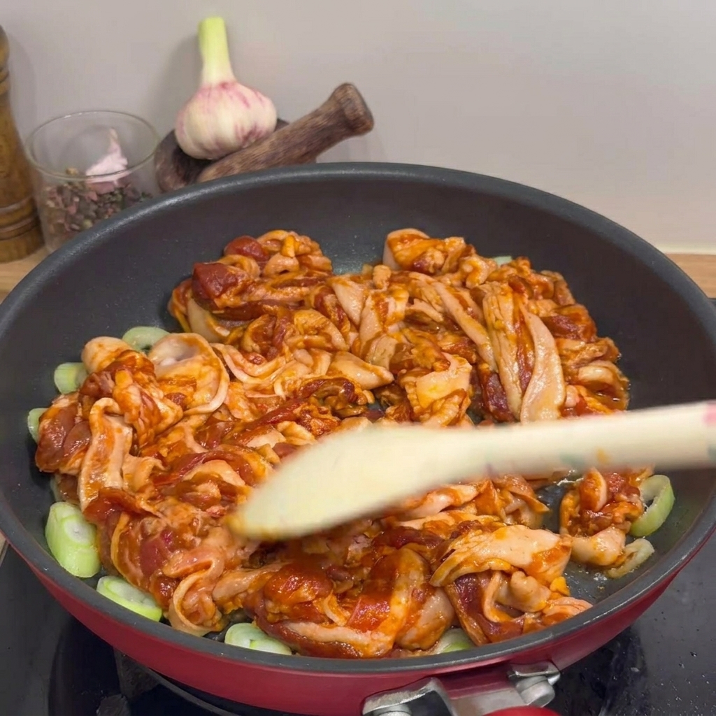 팬에서 노릇노릇하게 익어가는 삼겹살을 조리도구로 뒤집으며 볶는 모습