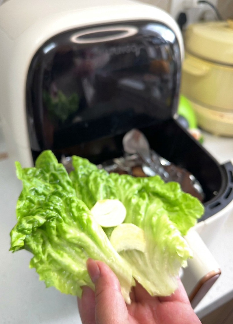 선명한 초록빛 상추 위에 얇게 썬 마늘 두 조각과 적양파 링이 올려진 모습을 손으로 들고 있는 사진.