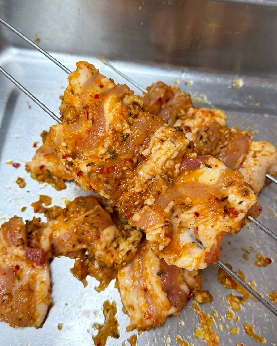 양념된 삼겹살을 두 개의 금속 꼬치에 나란히 끼우는 과정.