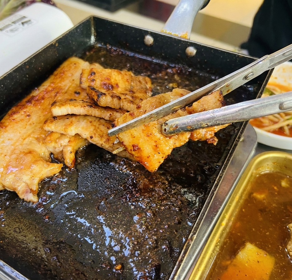가위를 사용해 노릇하게 익은 고기를 한입 크기로 자르는 모습.