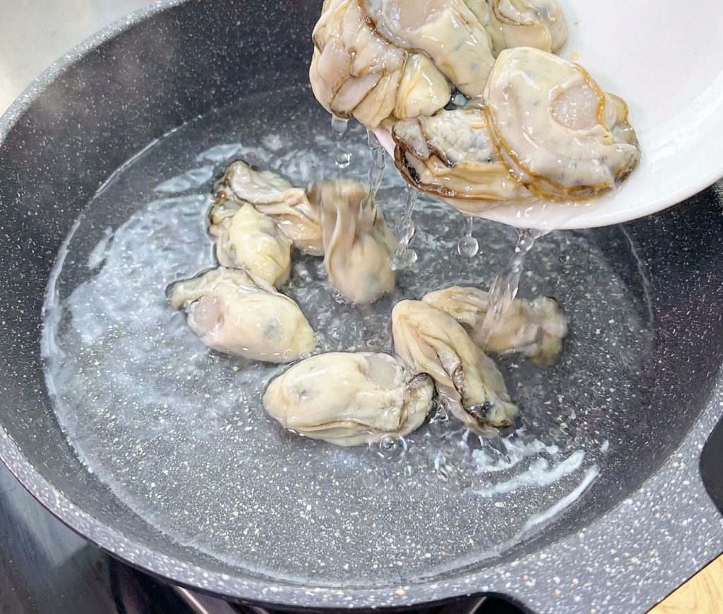 흰 접시에 담긴 신선한 생굴을 찬물이 담긴 워크 속으로 붓는 모습.