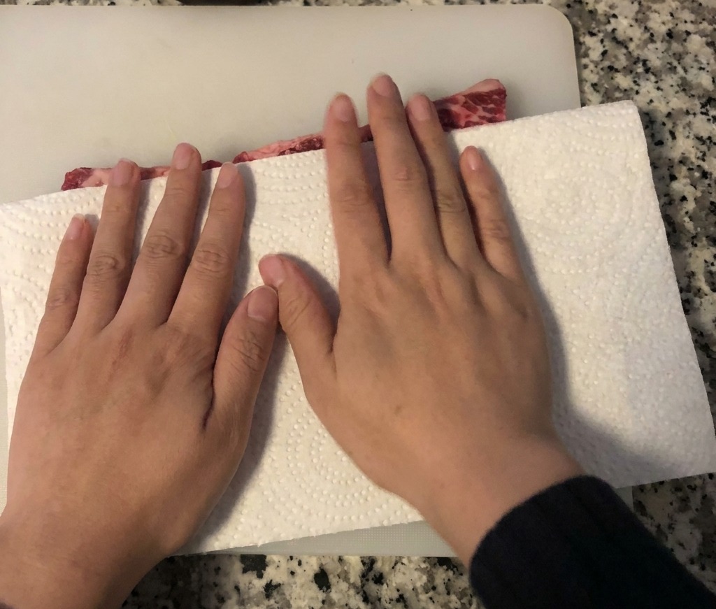 흰색 도마 위에 놓인 생 소갈비의 물기를 키친타월로 닦아내고 있는 모습
