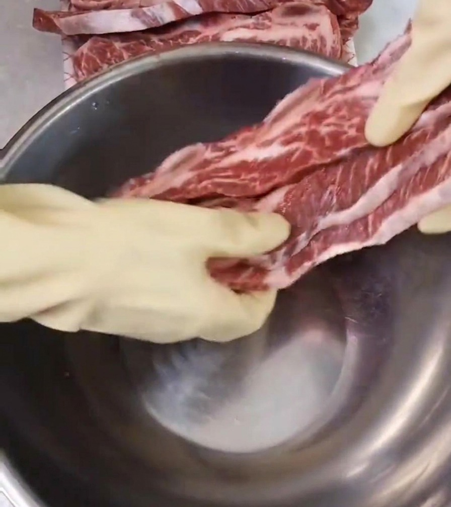흰 장갑을 낀 사람이 신선한 소갈비를 커다란 스테인리스 볼에 담고 있는 모습