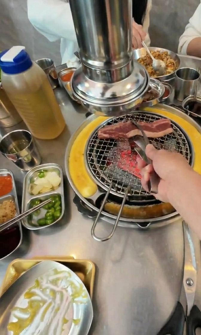 반찬들이 차려진 가운데 뜨거운 숯불 불판 위에 선홍빛 소갈비를 올리는 모습.