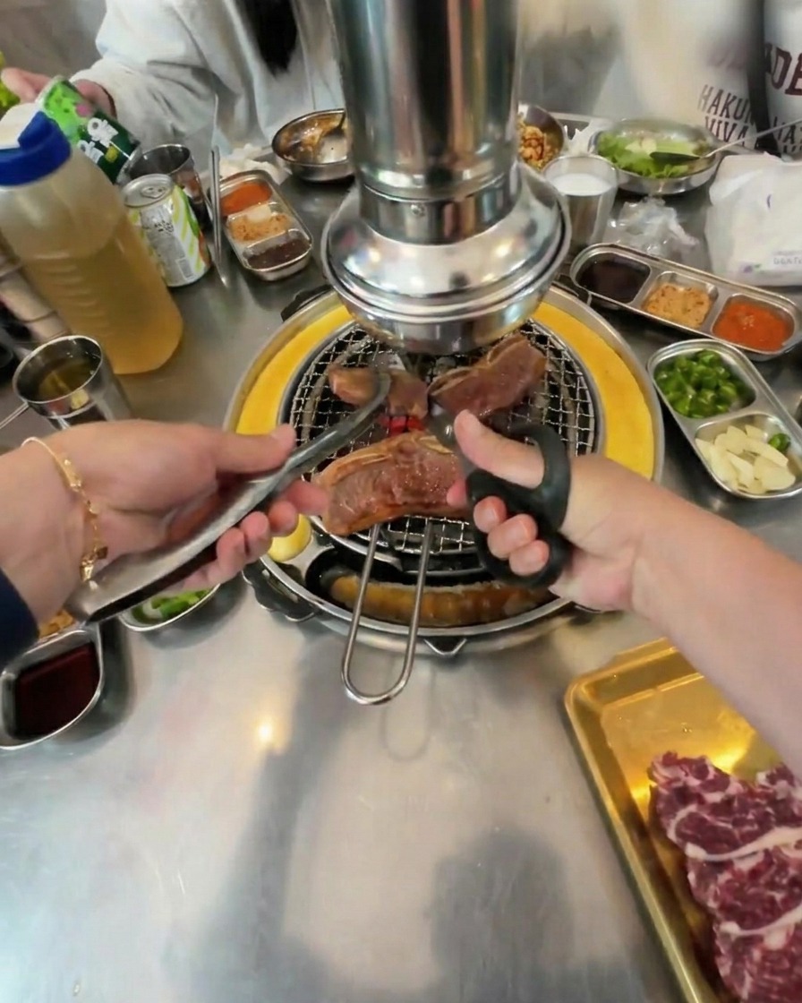 가위와 집게를 사용하여 불판 위의 갈비를 큼직하게 자르는 모습.