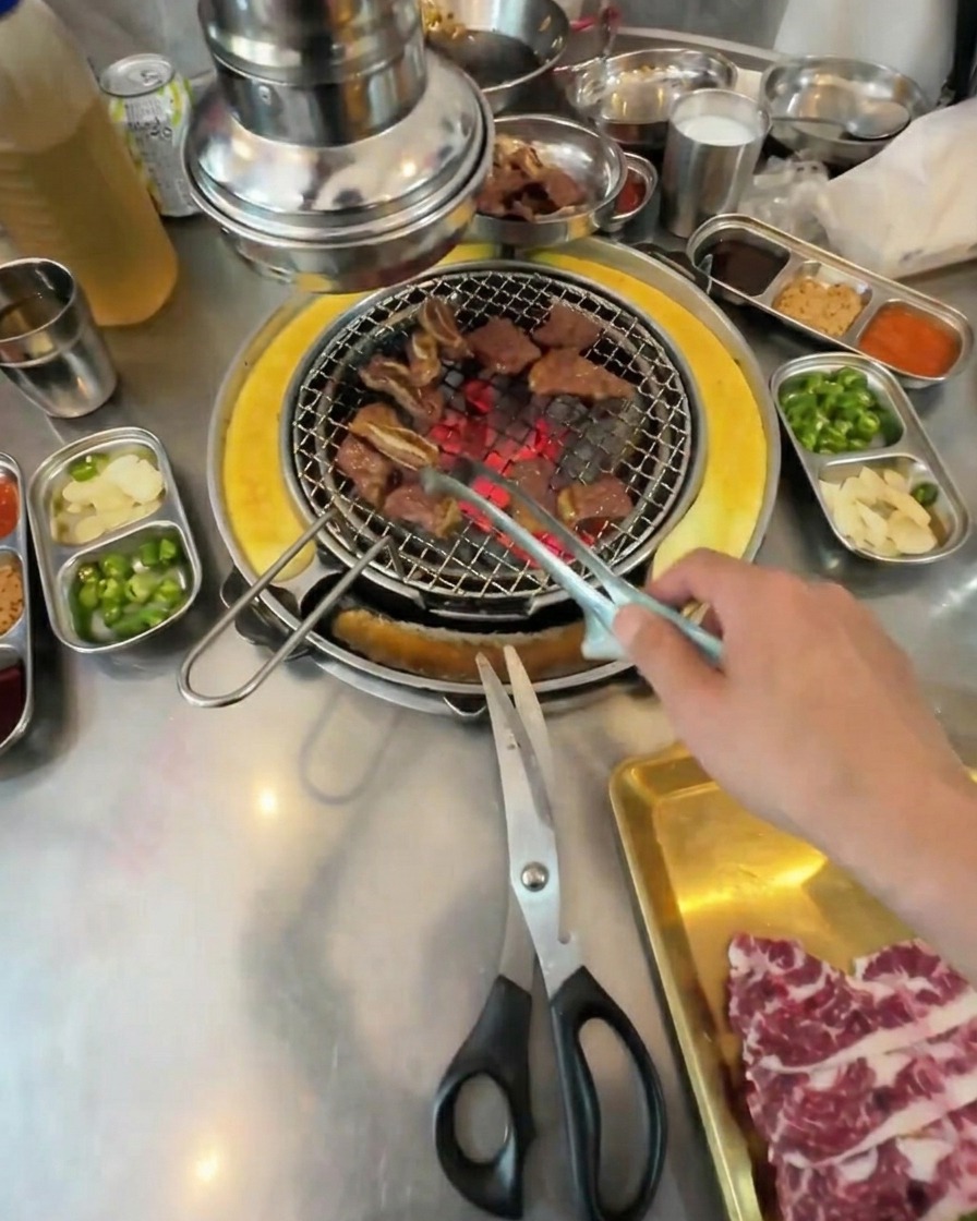 완전히 익어 지글거리는 갈비 조각들을 집게로 섞으며 굽는 모습.