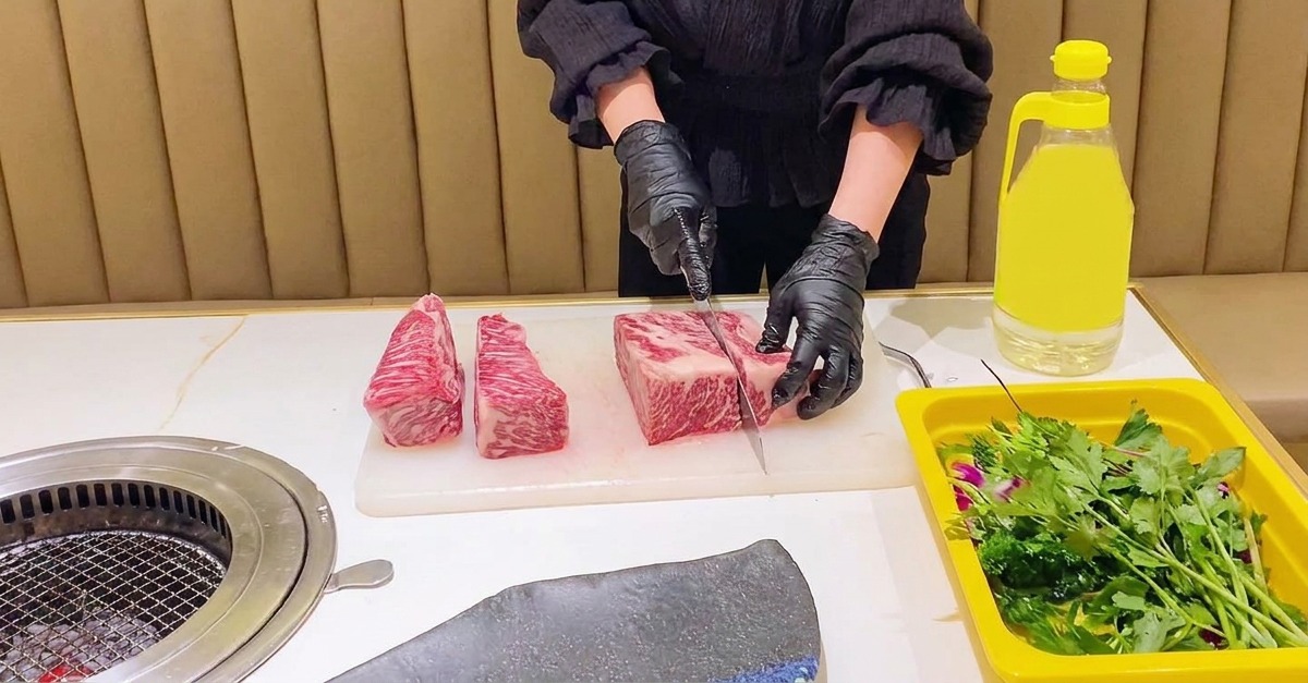 검은 장갑을 낀 요리사가 도마 위에서 마블링이 좋은 소갈비를 일정한 직사각형 모양의 블록으로 나누는 모습.