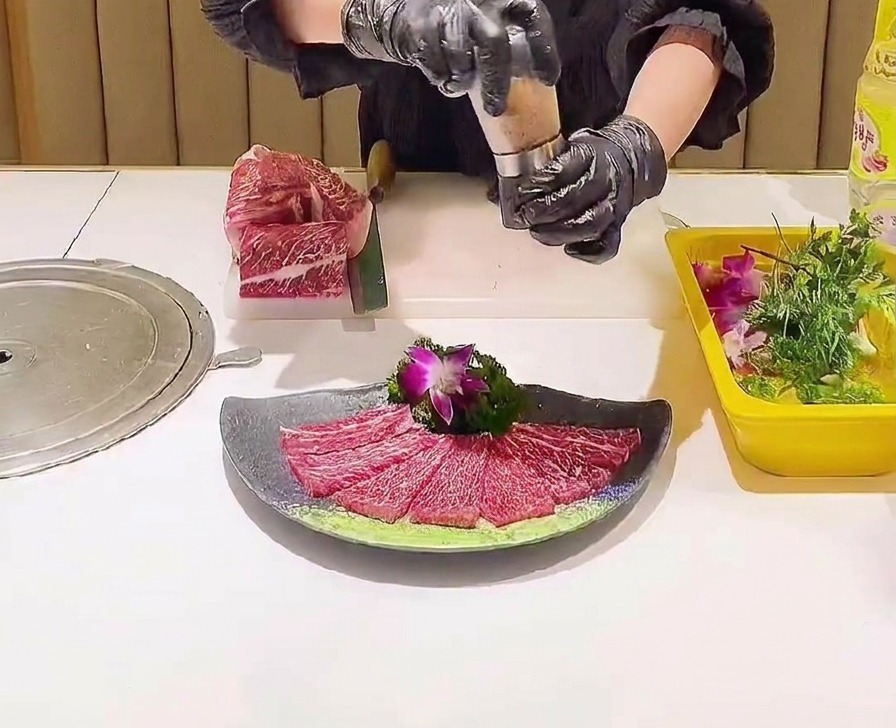 플레이팅이 완료된 소고기 위에 분홍색 소금 입자를 뿌리는 소금 그라인더.