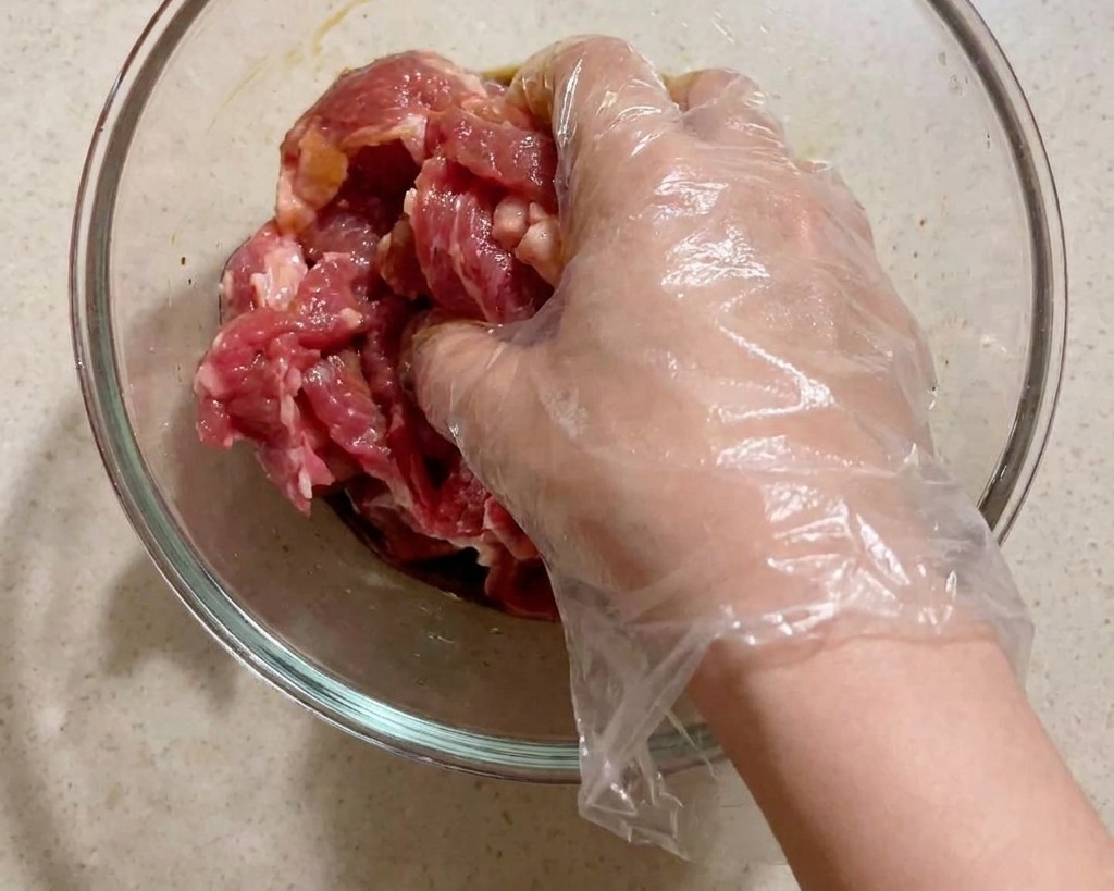 비닐 장갑을 낀 손으로 돼지고기와 양념을 골고루 버무리는 모습