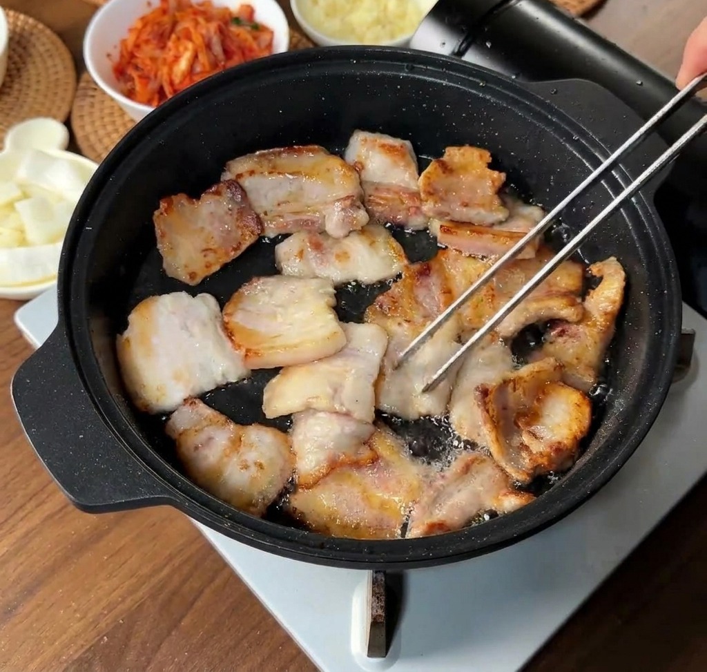검은 팬에서 삼겹살이 노릇하게 익어가는 모습