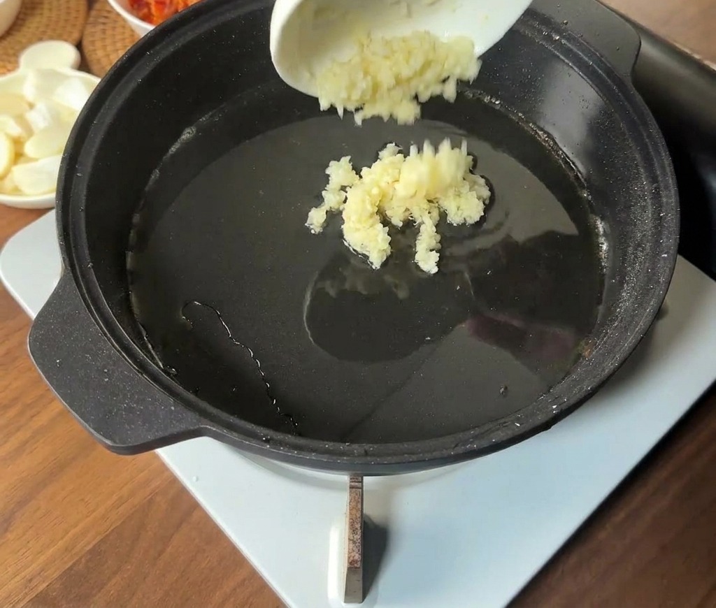 다진 마늘을 뜨거운 기름이 있는 팬 중앙에 붓는 모습