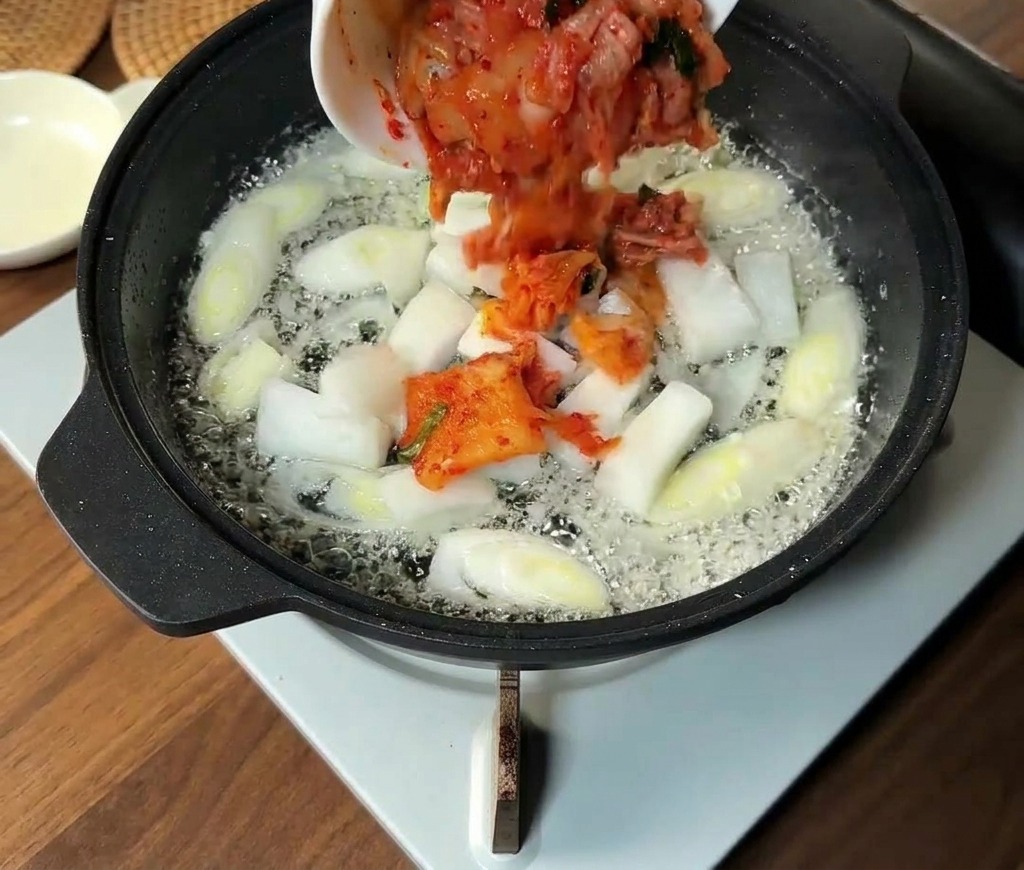 다진 김치와 채 썬 양파를 팬에 추가하는 모습