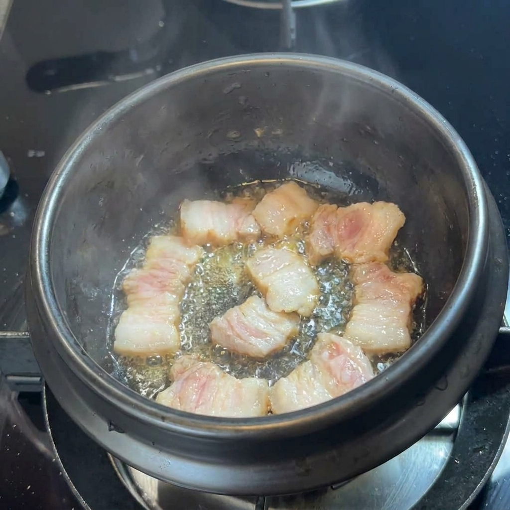 검은색 뚝배기 바닥에서 삼겹살이 기름을 내며 지글지글 익어가는 모습.