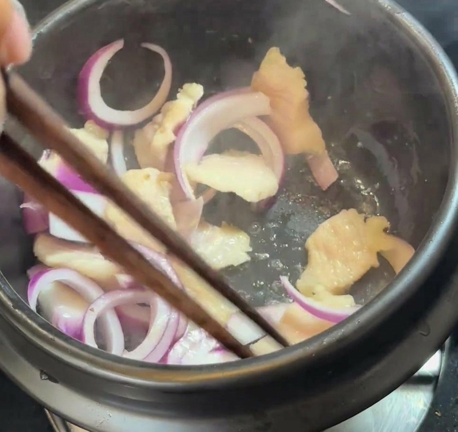 뚝배기 속 삼겹살과 돼지기름에 슬라이스한 적양파를 넣어 섞는 모습.