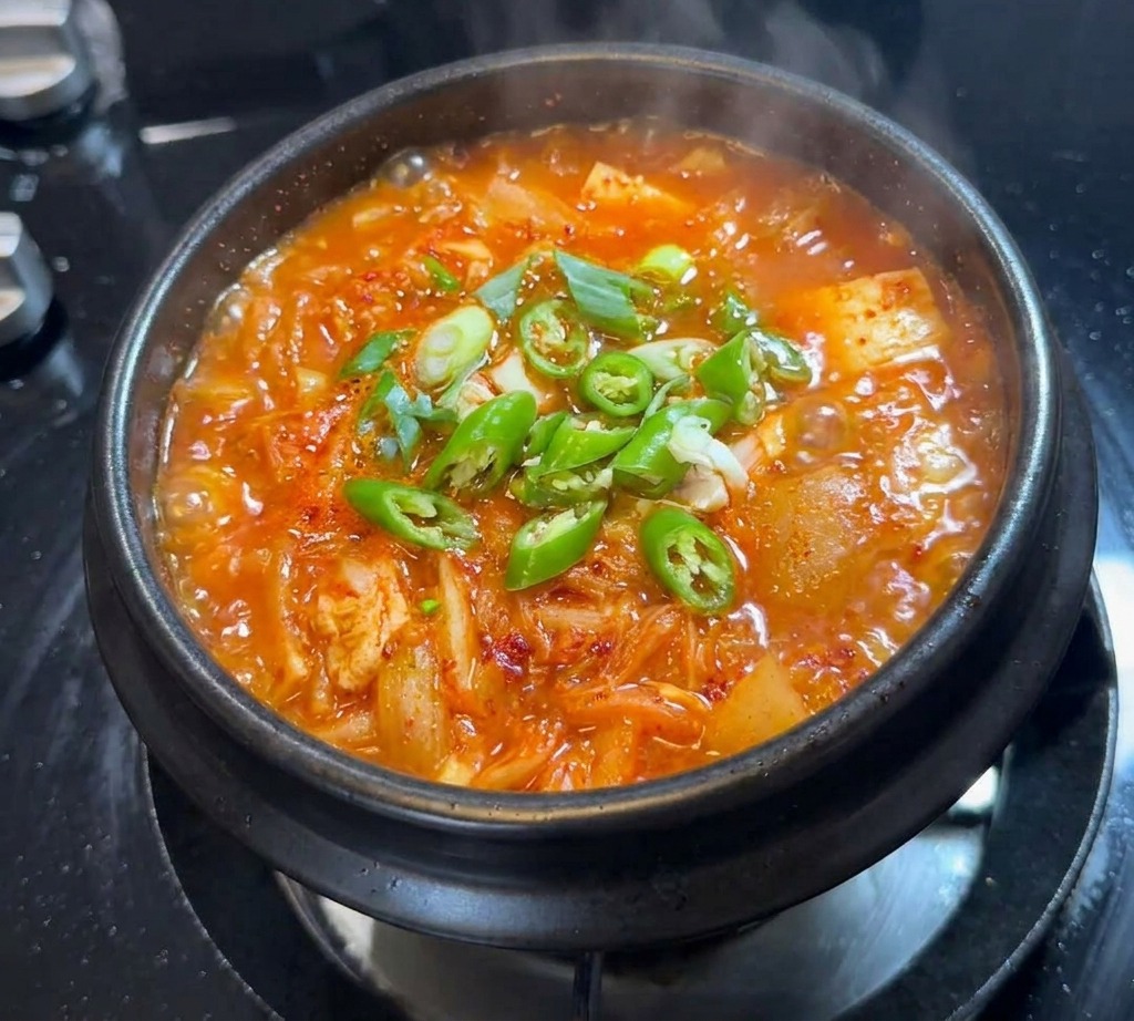 보글보글 끓는 김치찌개 표면에 썰어놓은 청양고추와 대파를 올린 모습.
