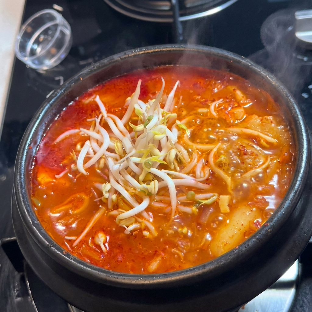 빨간 김치찌개 뚝배기 위에 신선한 하얀 숙주를 수북이 쌓아 올린 모습.