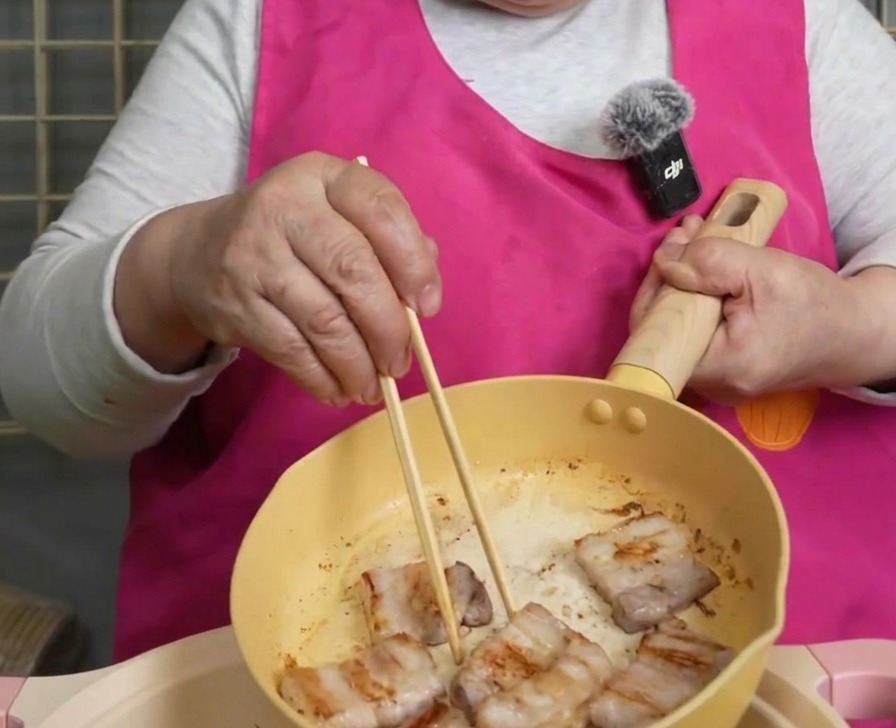 바삭하게 구워진 삼겹살을 젓가락으로 집어 찌개 냄비로 옮기는 모습