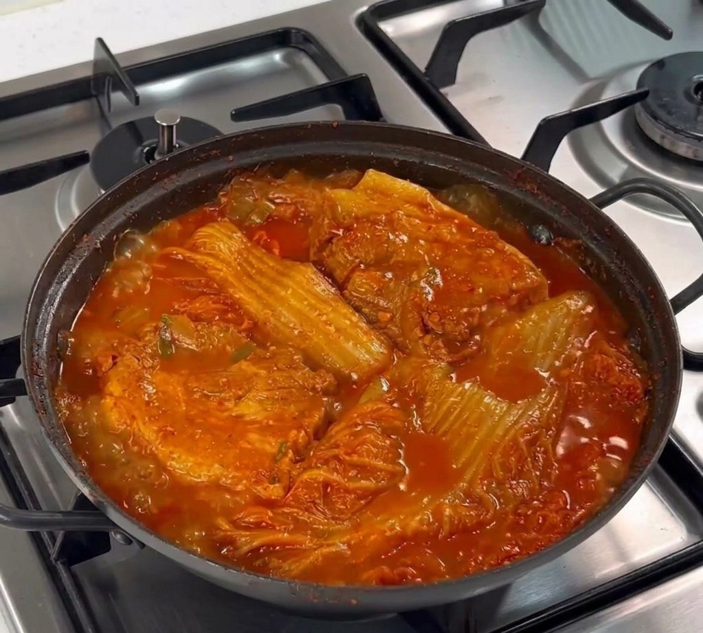 냄비 안의 생삼겹살 위에 숟가락으로 다진 마늘을 듬뿍 얹는 모습.