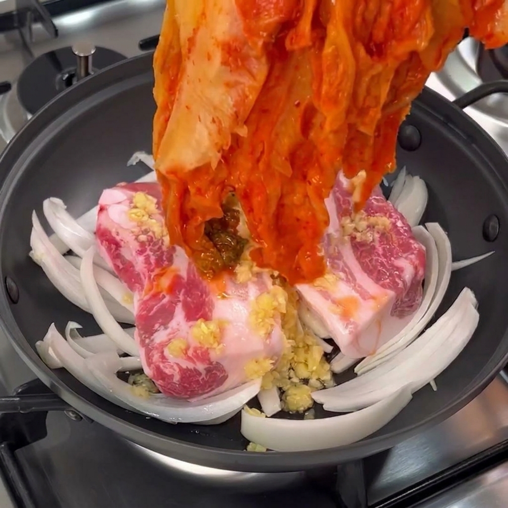 손으로 붉은 묵은지 한 포기를 통삼겹살 위에 넉넉하게 덮어주는 모습.