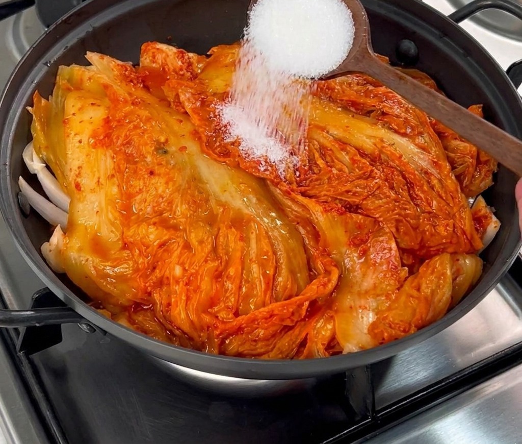 나무 숟가락으로 하얀 설탕을 김치 위에 고르게 뿌리는 모습.