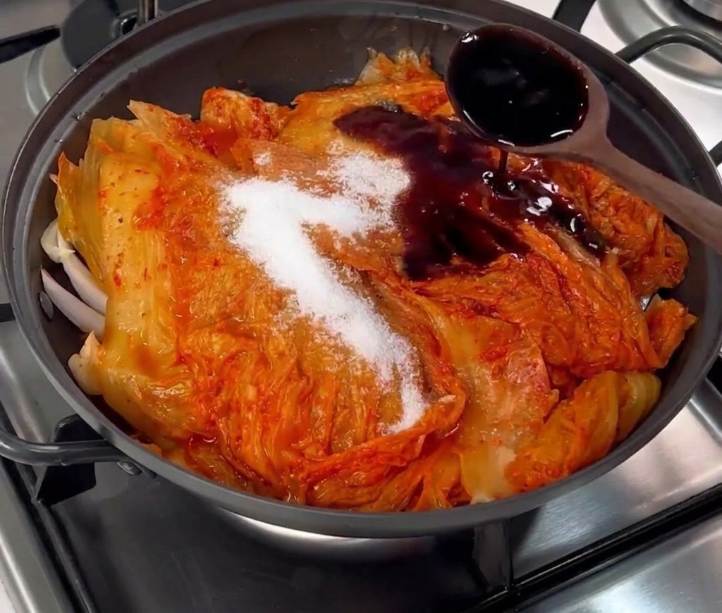 김치와 설탕이 올라간 냄비에 진간장을 부어 간을 맞추는 모습.