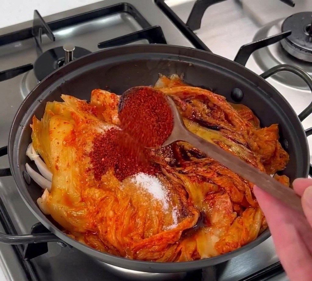 김치 위에 선명한 붉은색 고춧가루를 숟가락으로 뿌리는 모습.