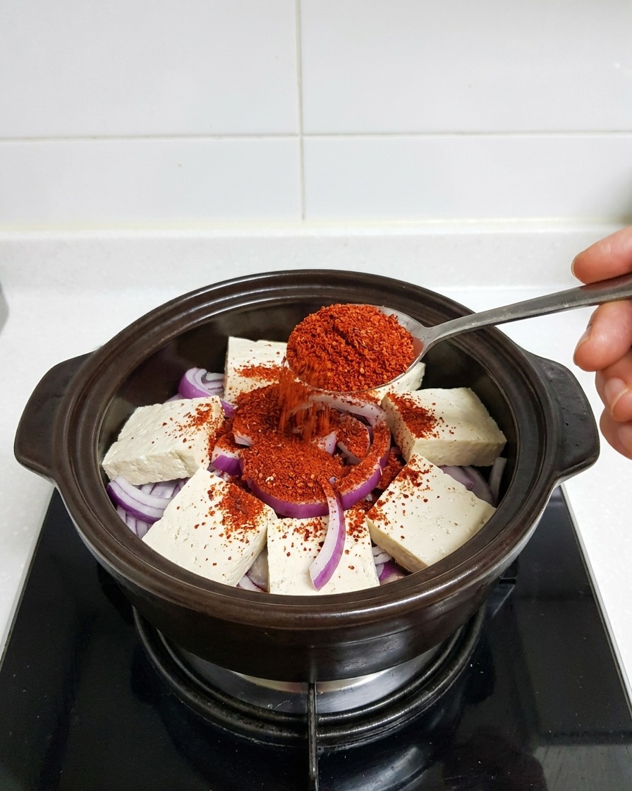 붉은 고춧가루를 찌개 재료 위에 넉넉히 뿌리는 모습