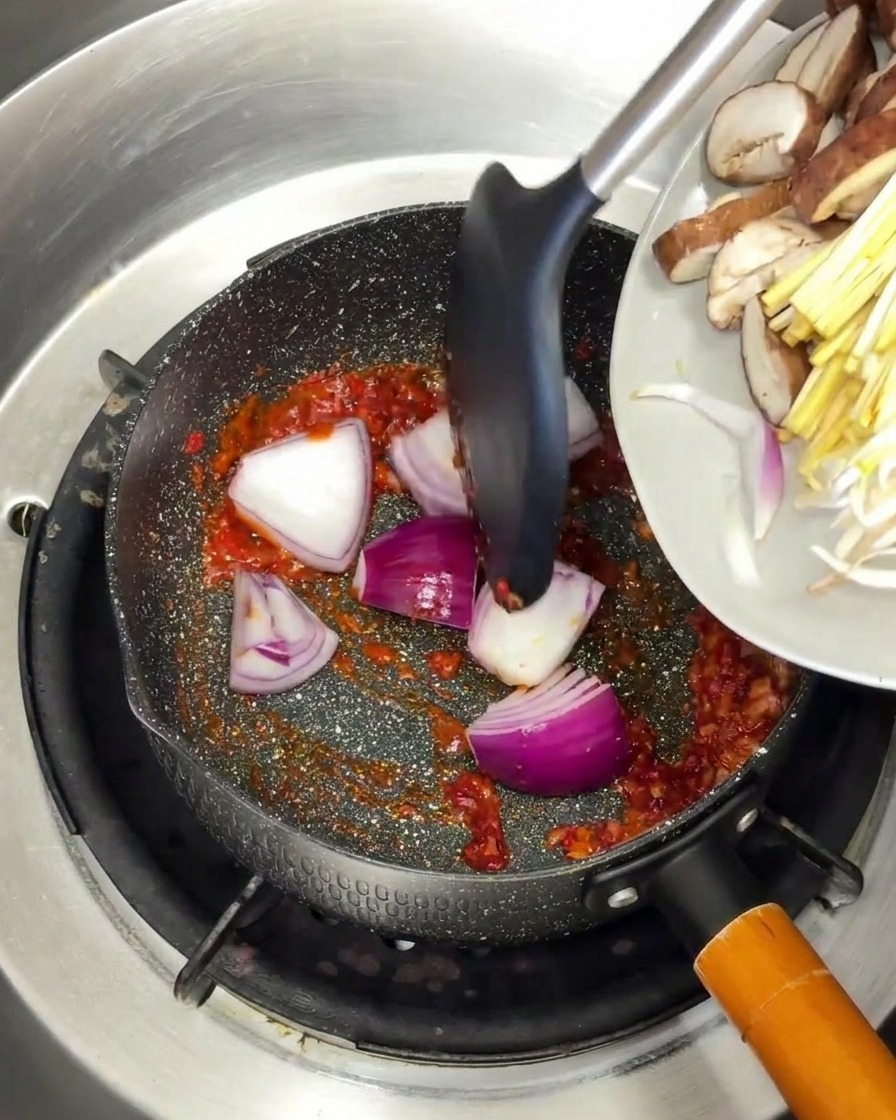 붉은 양념 베이스에 채 썬 적양파와 버섯을 넣고 골고루 섞으며 볶는 모습.