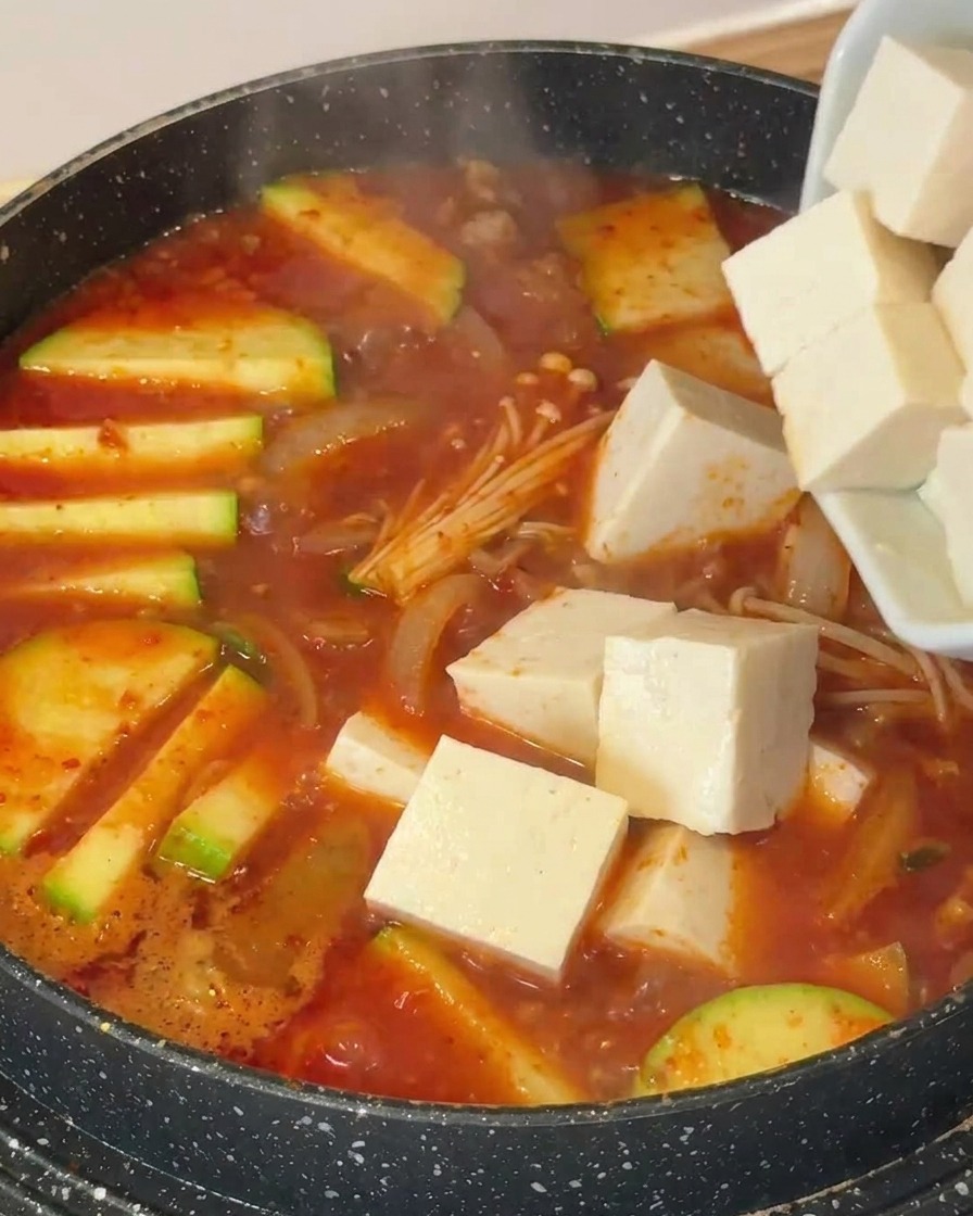 애호박과 버섯이 들어간 찌개에 하얀 두부를 넣는 모습