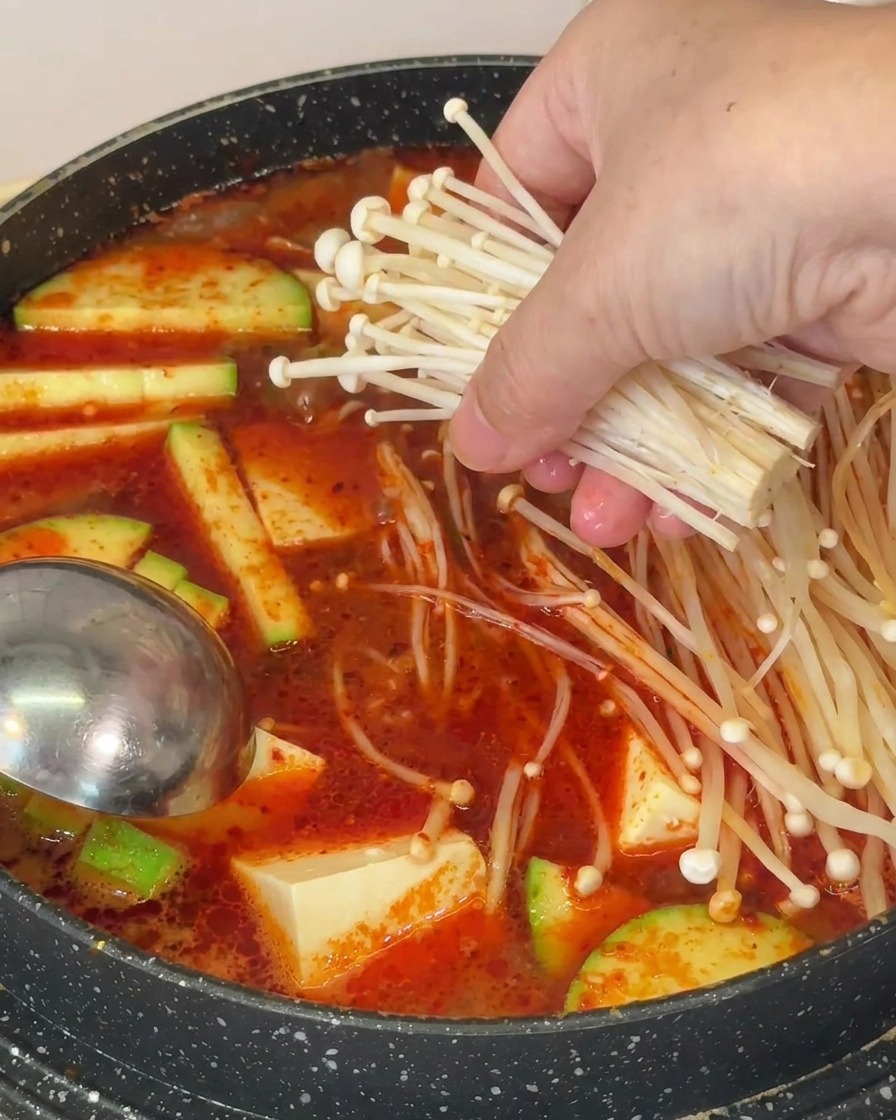 끓는 냄비에 팽이버섯 한 묶음을 넣는 손